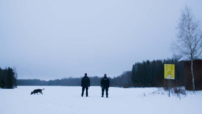 Kaksi hahmoa seisoo lumisella jäällä. Taustalla näkyy metsää.