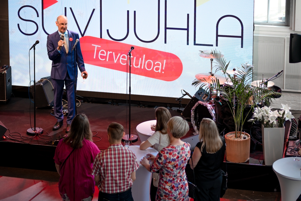 Kopioston eläköityvä varatoimitusjohtaja Jukka-Pekka Timonen seisoo lavalla ja puhuu mikrofoniin. Viisi ihmistä katselee häntä ja kuuntelee.